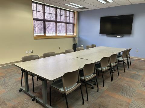 Tables and chairs in a meeting room with a television screen on the wall.