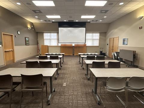 Meeting room with 6 tables and 2 chairs per table facing a projection screen.