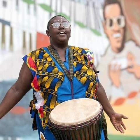 Person in African-style dress with a djembe drum.